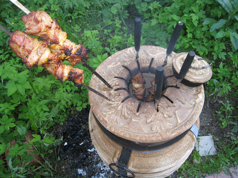 В керамическом тандыре жарятся шашлыки на шампурах